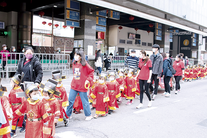 金城鎮寶貝園地幼兒園近百位戴著口罩、淘氣可愛的「小小財神」在金城市區沿街拜年，加上熱鬧的音樂聲，讓忙碌的市場洋溢著濃濃的年味和喜氣。（莊煥寧攝）