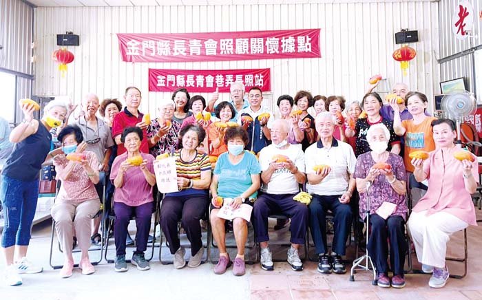 金城鎮民代表許燕輝前往金門縣長青會照顧關懷據點關心長者供餐執行情形,除感謝志工為社區供餐的付出,也致贈當令水果為老者加菜,並和長者開心合照。(金門縣長青會提供)