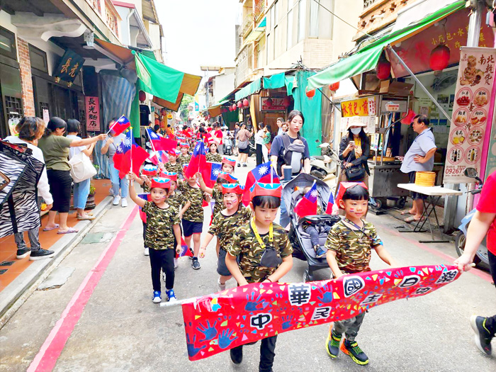 寶貝園地昨日前往金城街頭遊行,手拿國旗頭戴國旗帽,一起慶祝國慶日。(許峻魁攝)