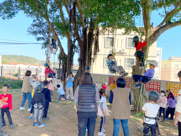 金門大學敏捷攀樹社攜手上杉夏海專業團隊前進湖埔國小、正義國小校園推廣本然教育活動,小朋友體驗攀樹樂趣以及參與遊戲。(金門大學敏捷攀樹社提供)