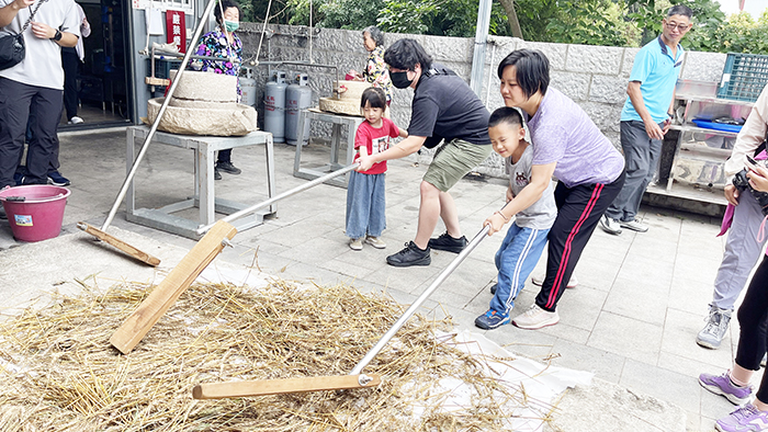 親子在志工帶領下,操作麥梳及「連耞」等農事工具。(陳麗妤攝)