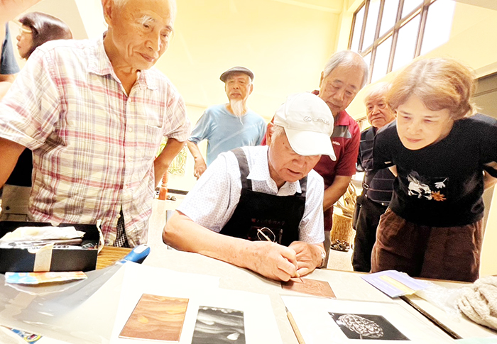 「臺灣現代版畫之父」廖修平博士(戴白帽者)細心指導美柔丁版畫創作。
(陳永富提供)