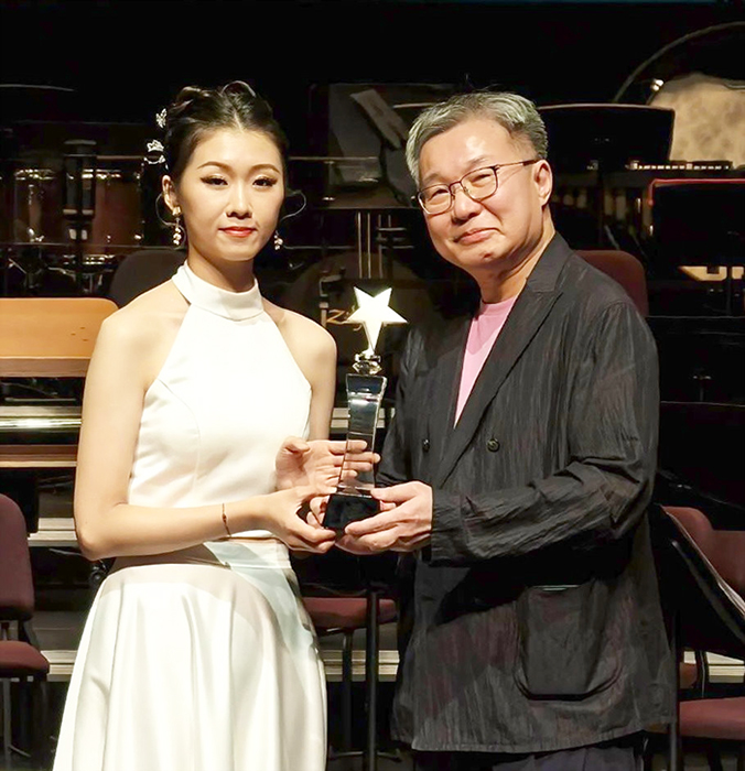 2026「NCO器樂大賽—《樂然指上》三弦新秀選拔」，金門女兒孫聿瑩（左）一舉拿下「第二名」及「最佳人氣獎」，接獲作曲家鍾耀光頒發獎項，象徵榮耀傳承。（孫聿瑩提供）