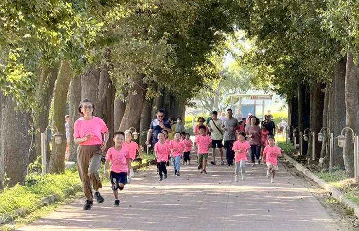 述美附幼陳高馨老師帶領幼兒園學童在楓香大道上衝刺返回校園。（李薇薇攝）