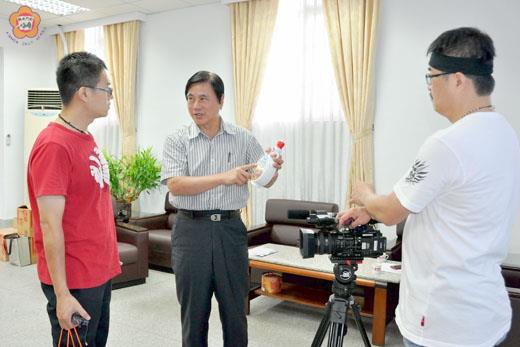 縣府秘書長盧志輝（中）接受大愛新聞記者訪問，並推銷金門高粱酒的特色。（莊煥寧攝）