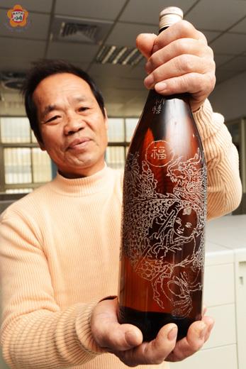  吳水源在酒瓶上刻出精彩的舞龍圖樣，並在展場中拿出各式酒瓶進行陳展。
（董森堡攝）