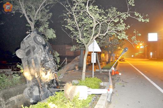 金沙環島北路昨日凌晨發生一起自撞車禍,路燈被連根拔起,自小客車頭近全毀,栽進排水溝中。(陳麗妤攝)