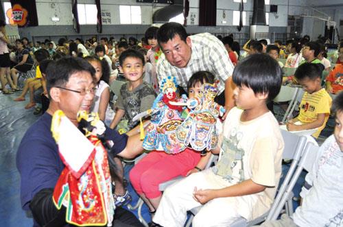 天宏園掌中劇團昨在寧中小演出,葉勢宏團長(左一)指導學童掌中技藝的表演要領。(李金鎗攝)