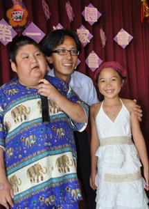 福田家園主任余國康、余彥臻陪著園生小胖威力上台獻唱。余彥臻利用暑假到福田擔任小志工。（張建騰攝）