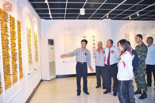   金門縣書法學會舉辦的大漢隸法書法展，昨日移地到烈嶼鄉文化館展覽：左、該會理事長洪明燦向鄉長洪成發、鄉代會主席洪若珊等來賓介紹作品特色；右、洪成發等人和參展者合影。（許加泰攝）