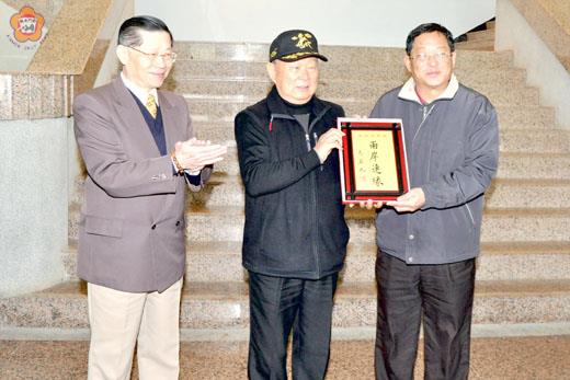 中華粥會「將軍書畫展」昨在文化局睿觀廳開展，丁之發名譽總會長（中）與陸炳文會長（左）代表致贈馬英九題詞的「兩岸連緣」紀念牌，由文化局長李錫隆代表接受。 （莊煥寧攝）